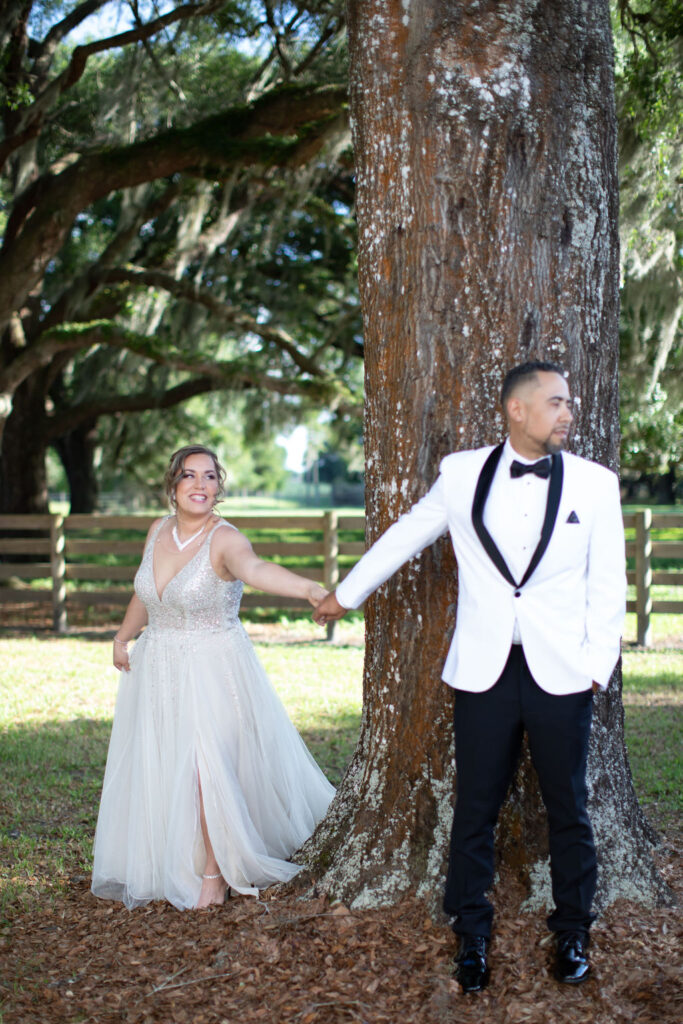 Bride and groom take first glimpse photos while holding hands around the large oak tree. 