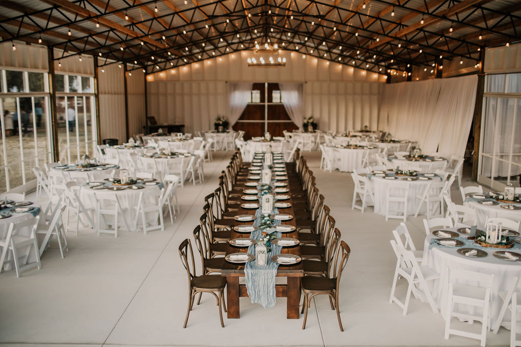Inside the big barn pavilion we are set up for 170 guests with round tables with white linens and four stained wooden farm tables with crossback chairs.  The backdrop is the solid front part of the barn showcasing the large stained barn doors.  The clear sliding vinyl doors keep out the wind and rain while allowing unobstructed views of the open pastures.  