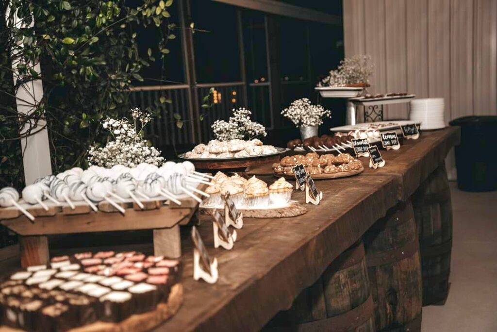Brown whiskey barrels with rustic wood tops to create a table type setting filled with an assortment of yummy desserts.