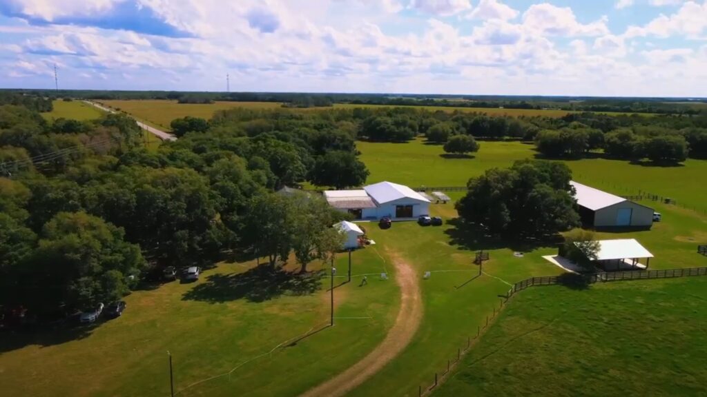 Aerial view of the farm.  Green pastures and large oak trees.  Our Big Barn Pavilion, home and barns dot the landscape.  It is a beautiful sunny day.