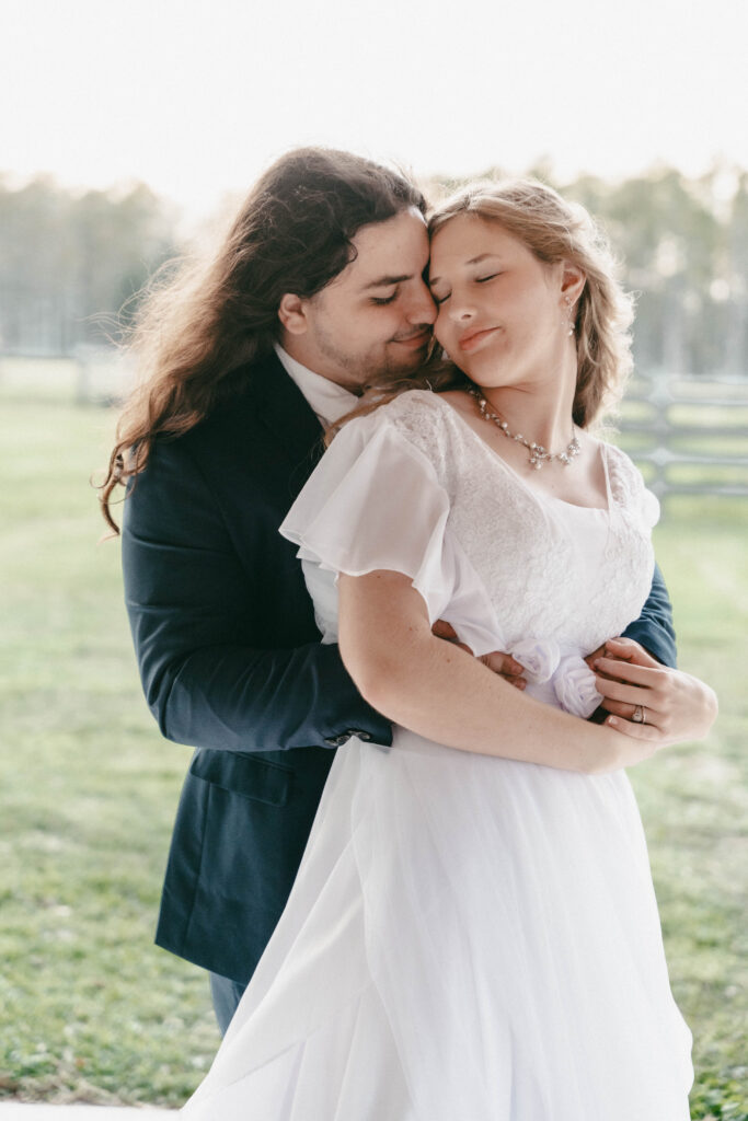 Newly wedded couple share an embrace. He is standing behind her with his hands around her waist. She has turned her head to meet his as they share an intimate moment on the Heart D Farm Wedding Venue